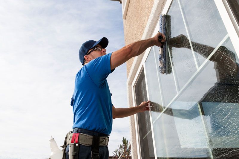 A Chesapeake Hydro-Wash technician in uniform professionally cleans an exterior residential window with a mop-style tool, ensuring a streak-free finish.