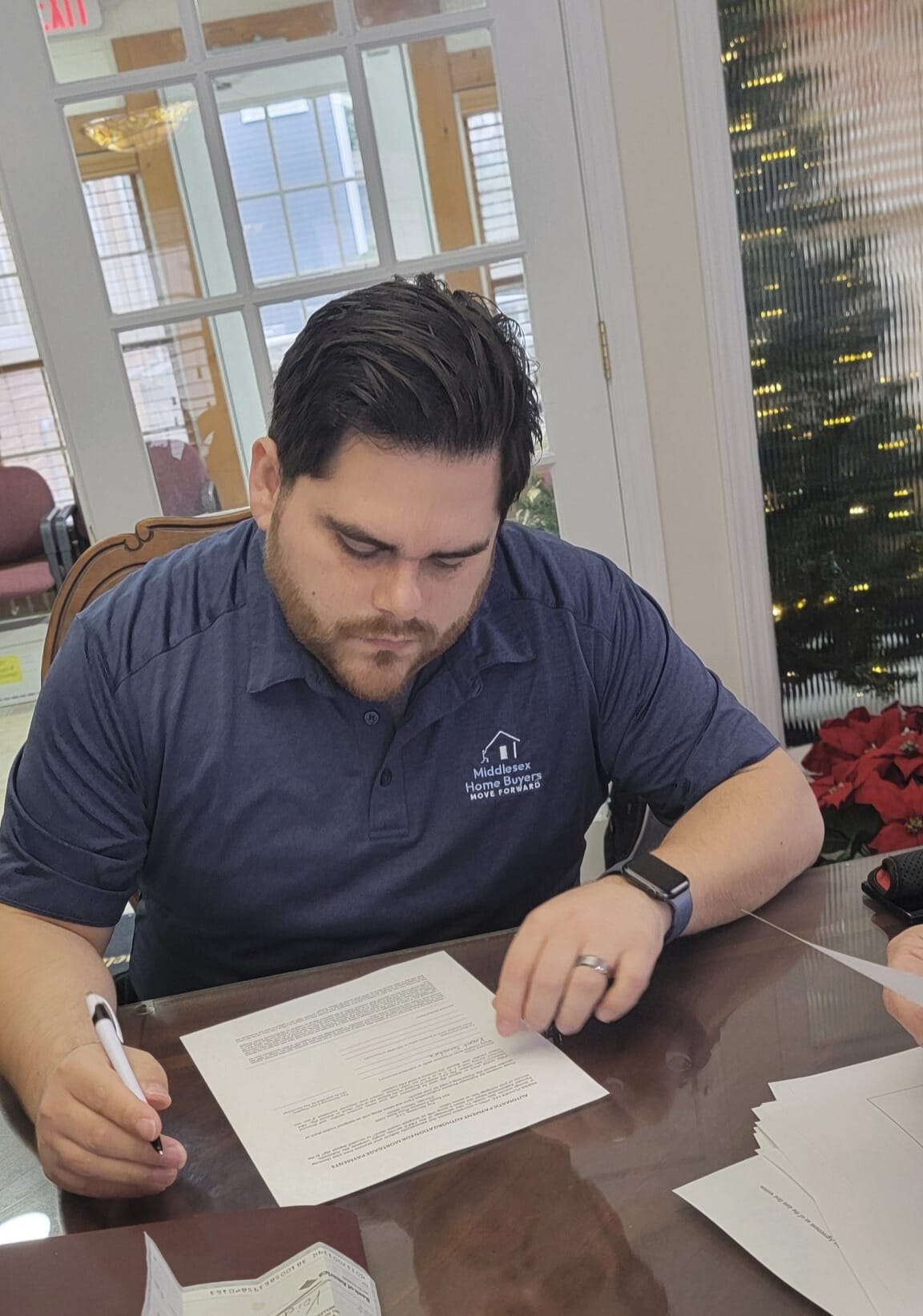 A Middlesex Home Buyers team member reviews and signs purchase agreement documents at a desk