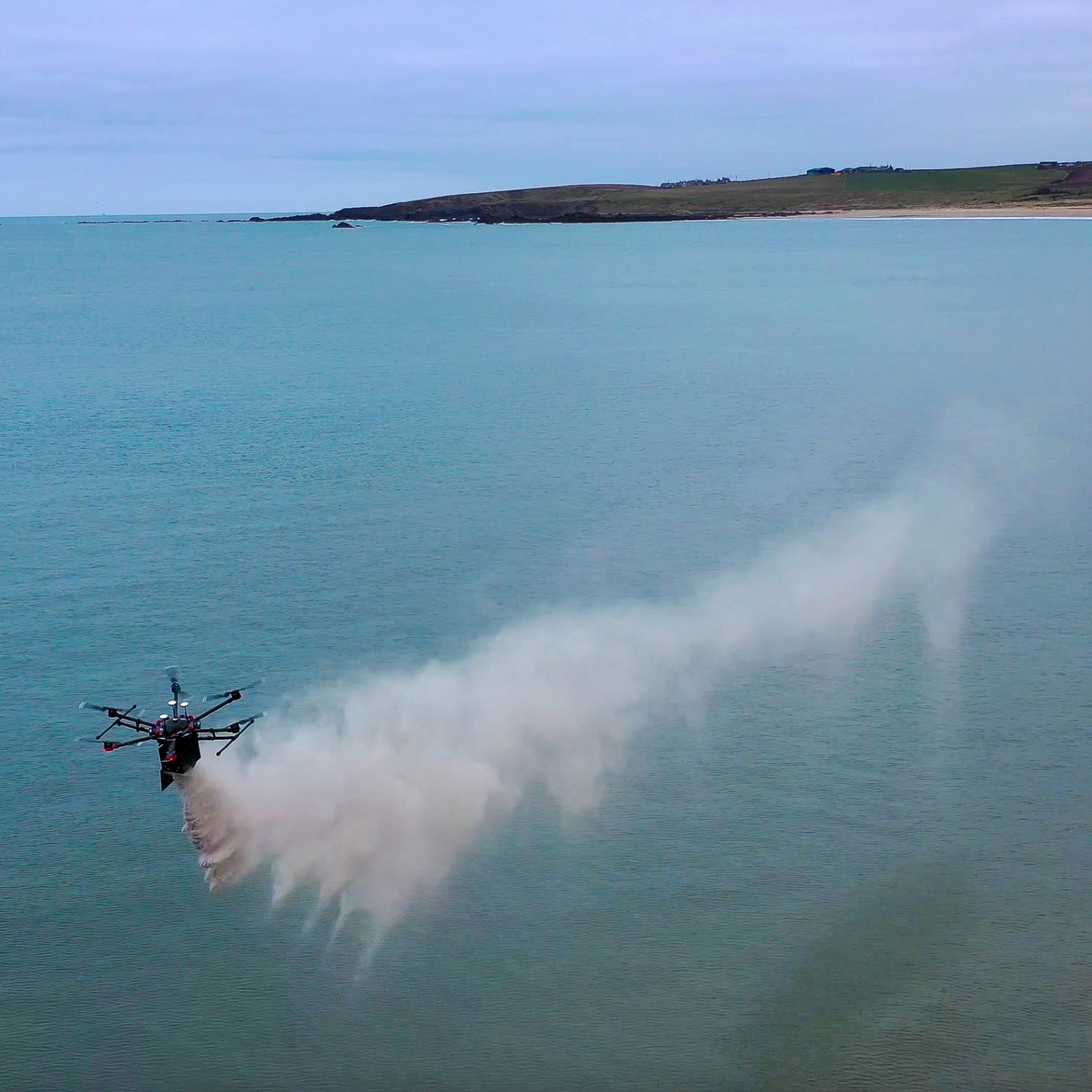 A multi-rotor drone scatters cremated ashes over calm coastal waters