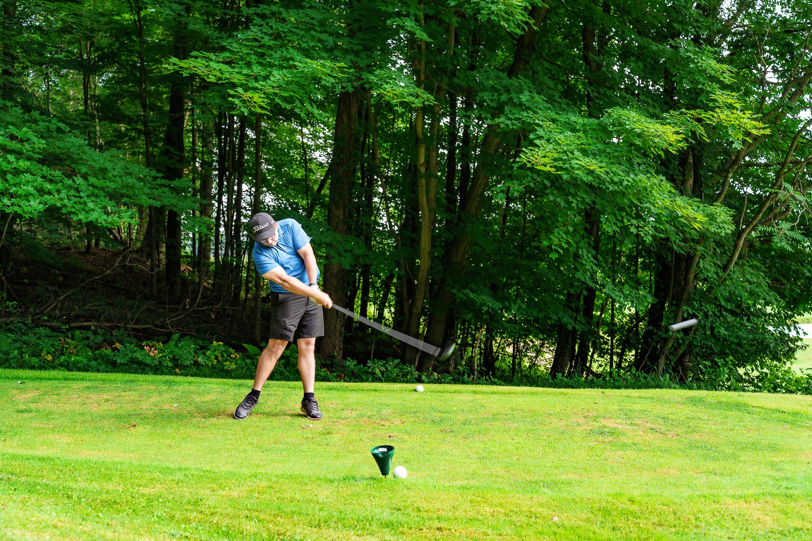 A man in a blue shirt and black shorts mid-swing on a golf course