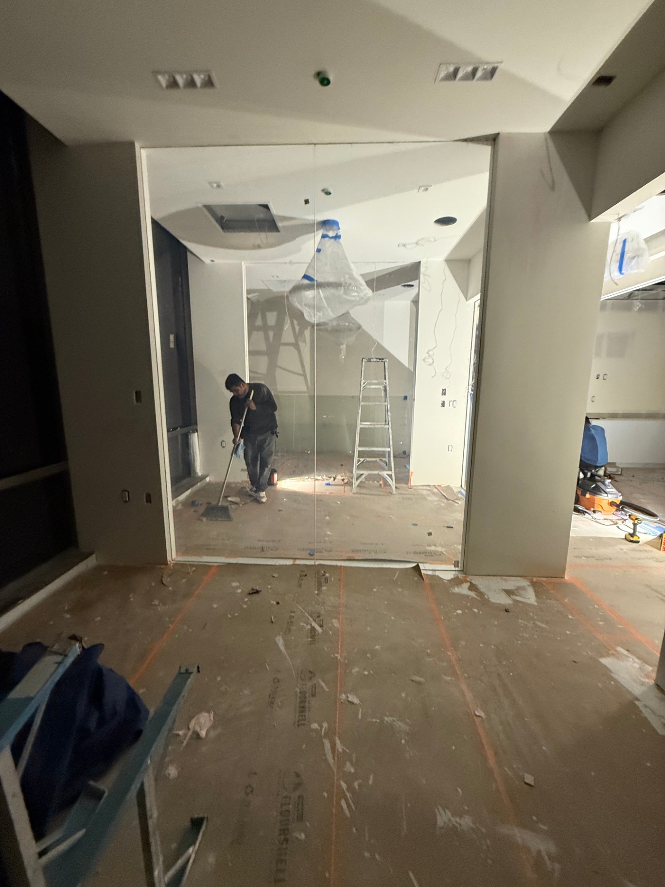 Office Smart Glass Partition Installation Office under renovation with a large, edge-to-edge smart glass partition installed by our team, ready for wiring and calibration. Workers are preparing the site for integration of our switchable PDLC film technology, ensuring future privacy-on-demand and optimal light management. Tools and protective coverings are visible, highlighting precision installation in a commercial space.