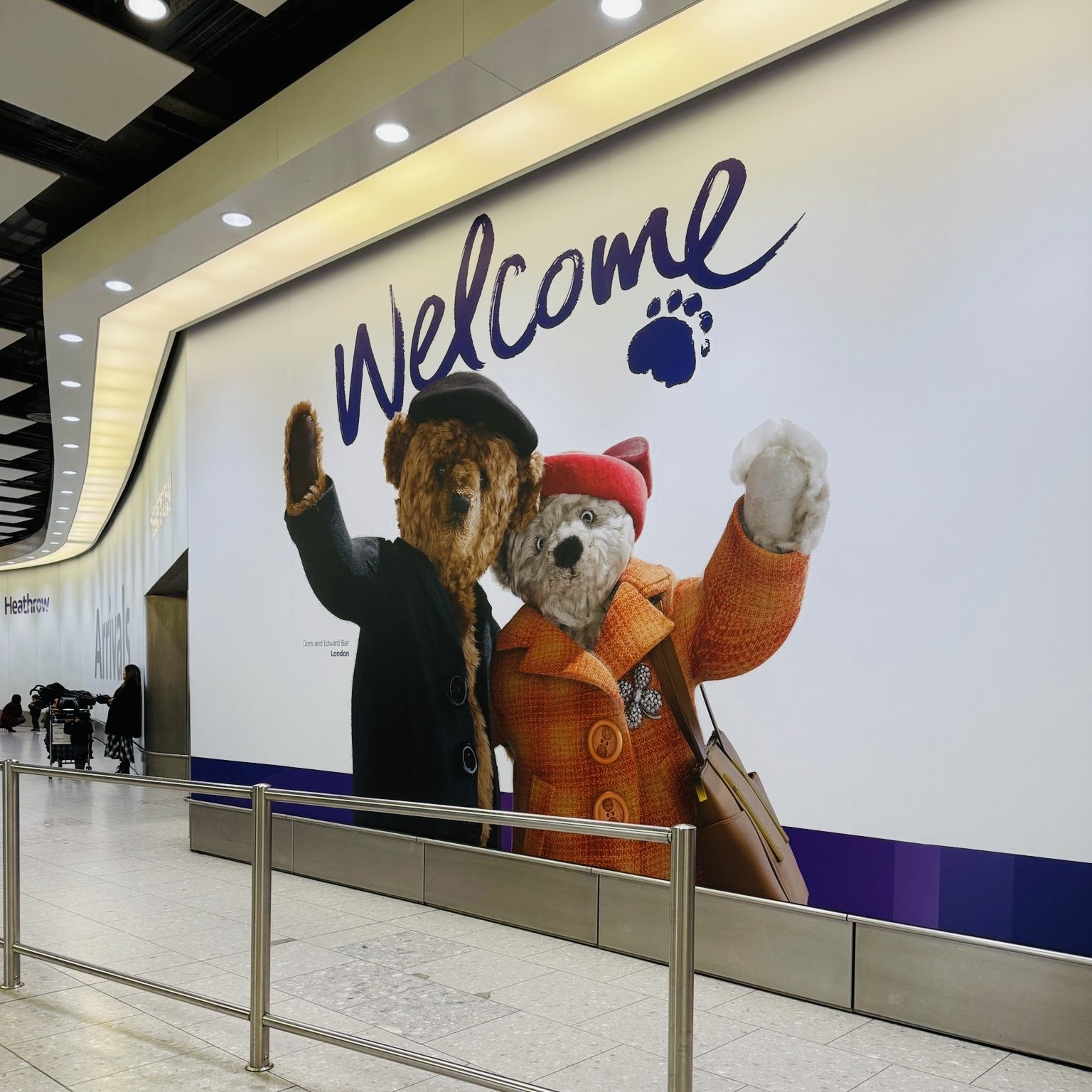 A welcoming scene at the Heathrow Airport arrivals area featuring a large 'Welcome' sign accompanied by friendly teddy bears.