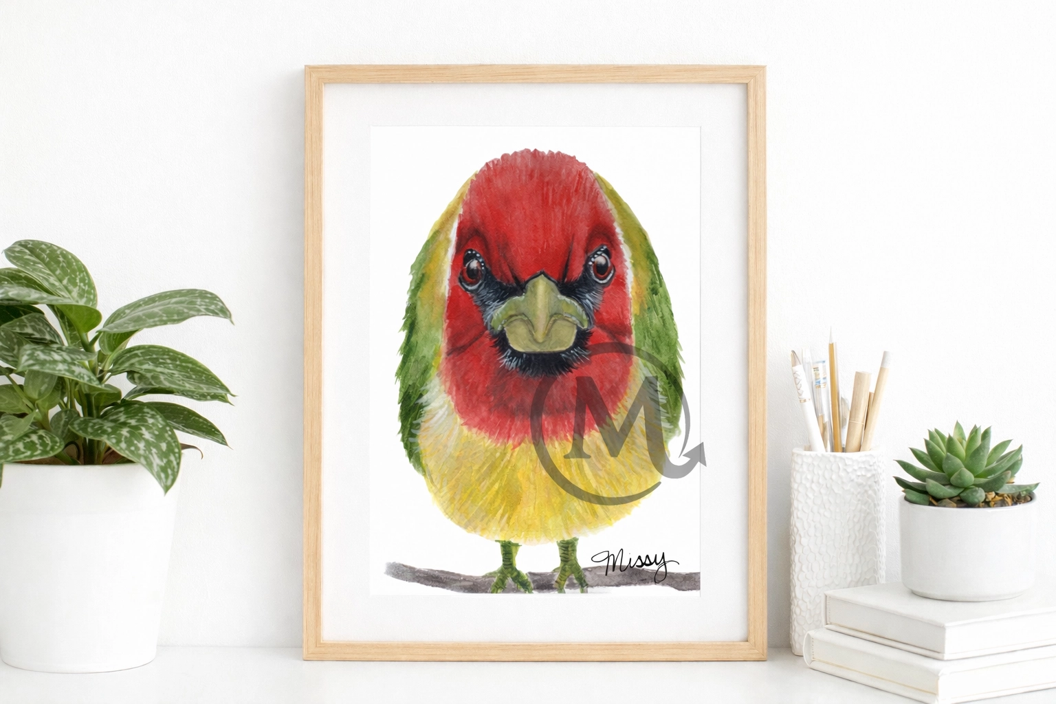 Missy’s original watercolor parrot artwork displayed in a styled light wood frame mockup on a minimalist white desk with plants, with the original watermark and signature fully visible.
