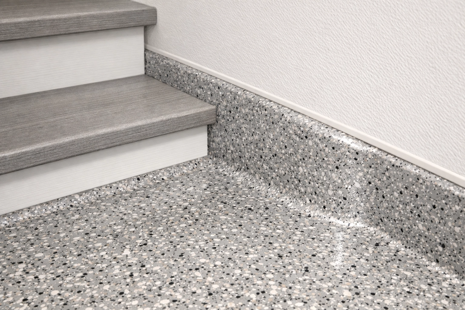 Expertly finished polyaspartic coating showing a seamless cove base and clean edges along garage stairs.